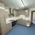 Modern kitchen with beige cabinets, stainless steel range hood, electric hob, oven, and double sink.