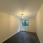 A bedroom with beige walls, grey carpet, window with curtain pole, and radiator beneath.