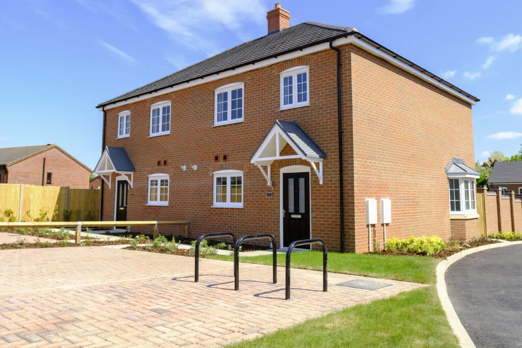 Front elevation of 7 & 9 Old Quarry Close, Metheringham showing a pair of completed brick semi-detached homes with black front doors, white-framed windows, pitched porch canopies, cycle stands and block-paved parking under a clear blue sky | Lafford Living