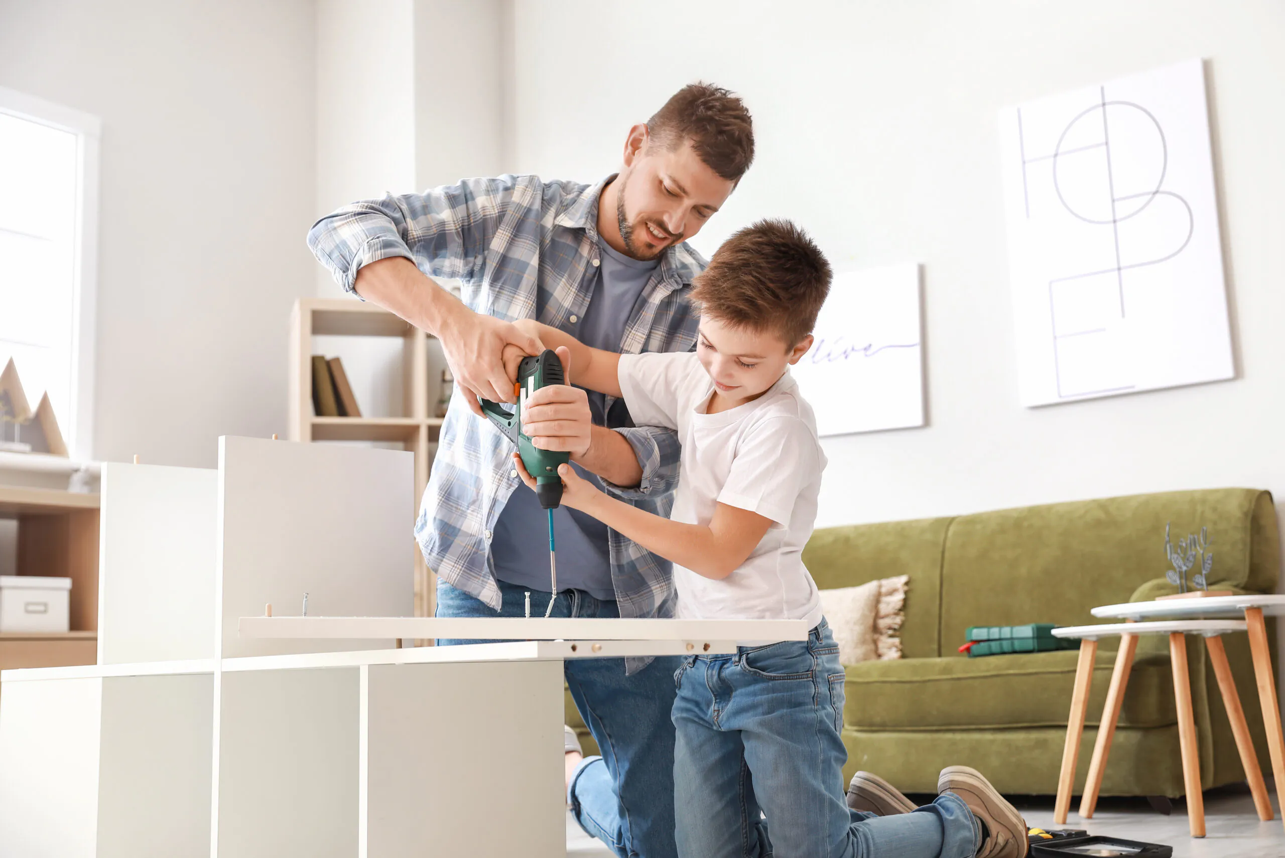 Father and son assembling flat-pack furniture using an electric drill in a living room | Lafford Group