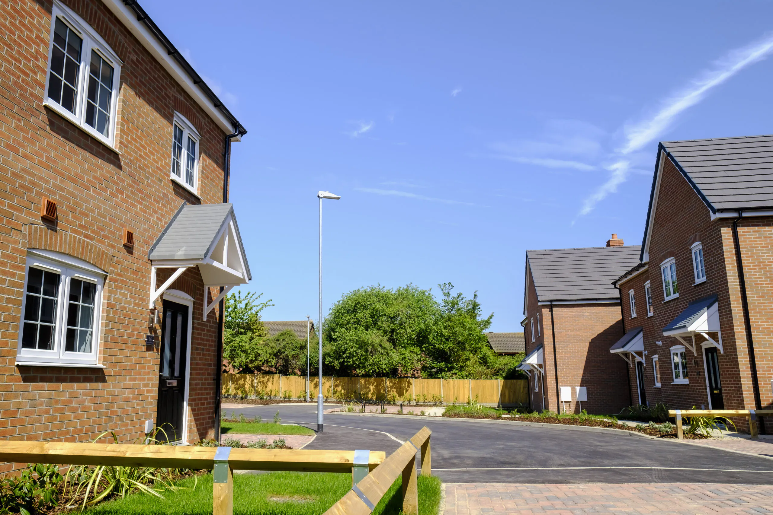 Street scene at Old Quarry Close, Metheringham showing completed brick homes, a curved new road, timber bollards, fresh planting and a central streetlamp under a clear blue sky | Lafford Group