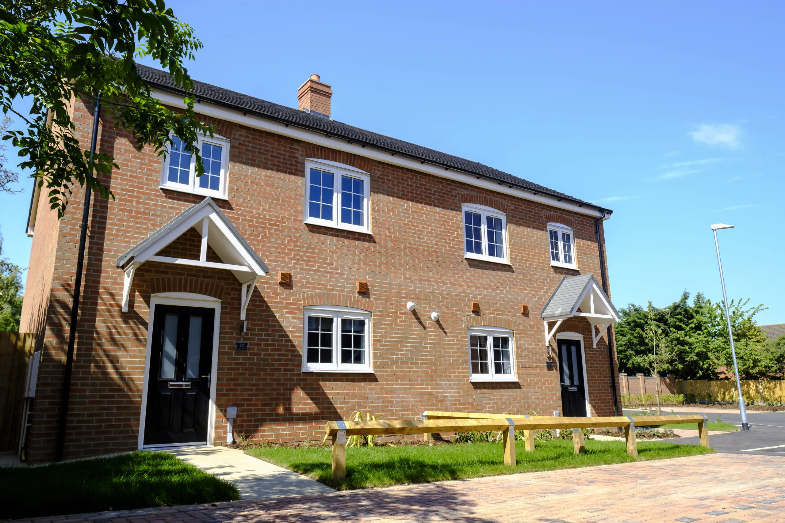 Front elevation of a completed brick home at Old Quarry Close, Metheringham with black front doors, white windows, small lawn and timber bollards under a clear blue sky | Lafford Living