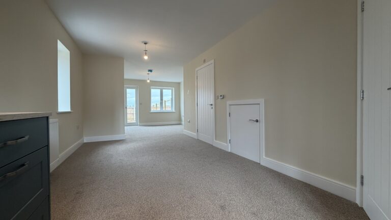 The Waltham at Petrella Place – view from the kitchen into the open-plan dining and living area with neutral décor, fitted carpet, pendant lights, and rear glazing including a door and window to the garden.