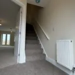 The Waltham at Petrella Place – entrance hallway with carpeted staircase, white handrail, radiator and doorway through to the open-plan living space with French doors beyond.