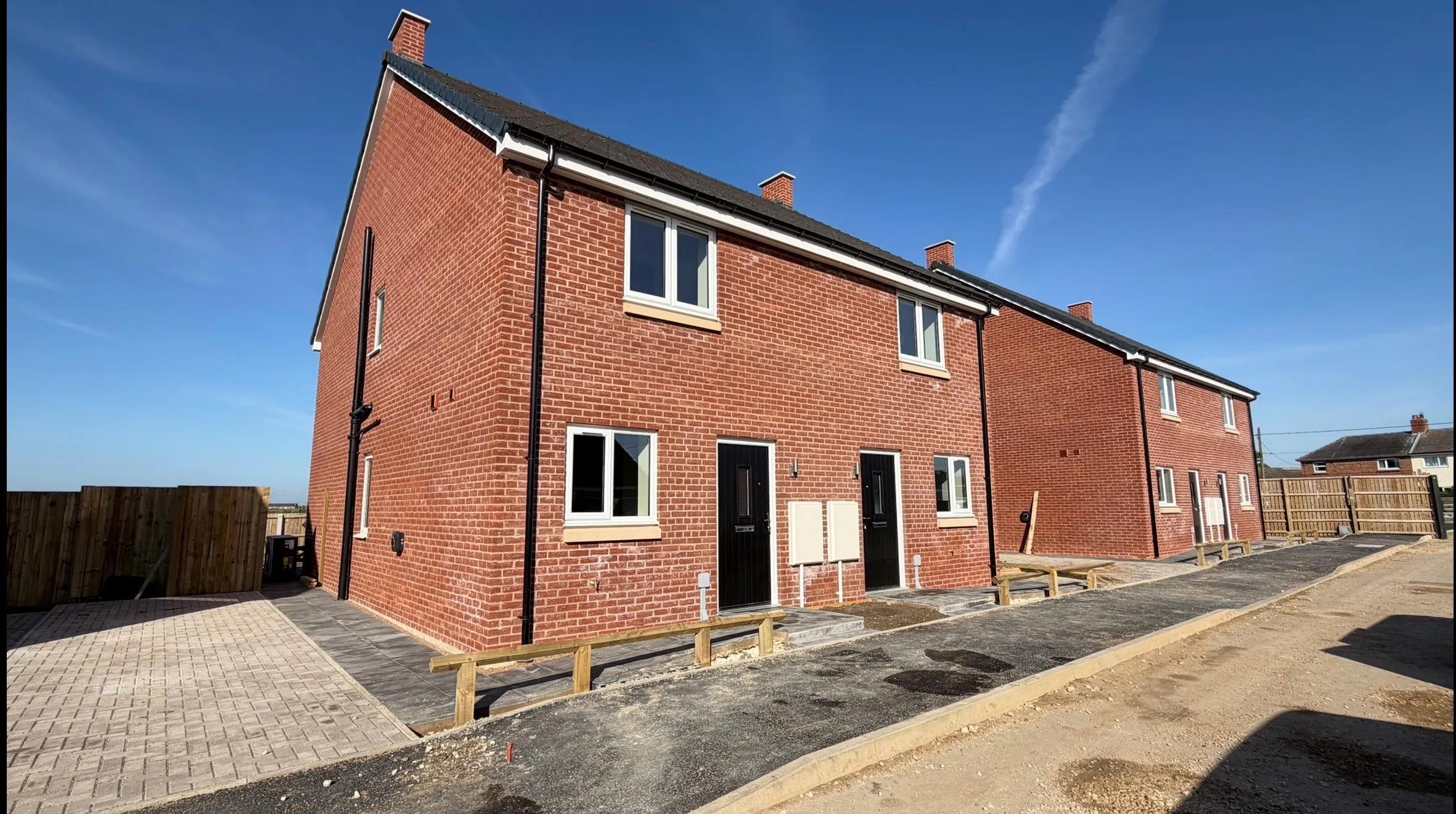 External street view at Petrella Place showing The Waltham Plot 19 on the left and Plot 20 on the right, with Plots 21 and 22 visible further along the row of new red-brick homes.