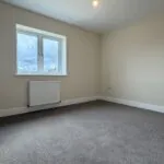 The Caister at Petrella Place – Bedroom 1 with neutral décor, fitted carpet, double window and radiator beneath.
