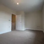 The Caister at Petrella Place – Bedroom 1 alternate view showing neutral décor, fitted carpet, large window with radiator below and the open door to the landing.