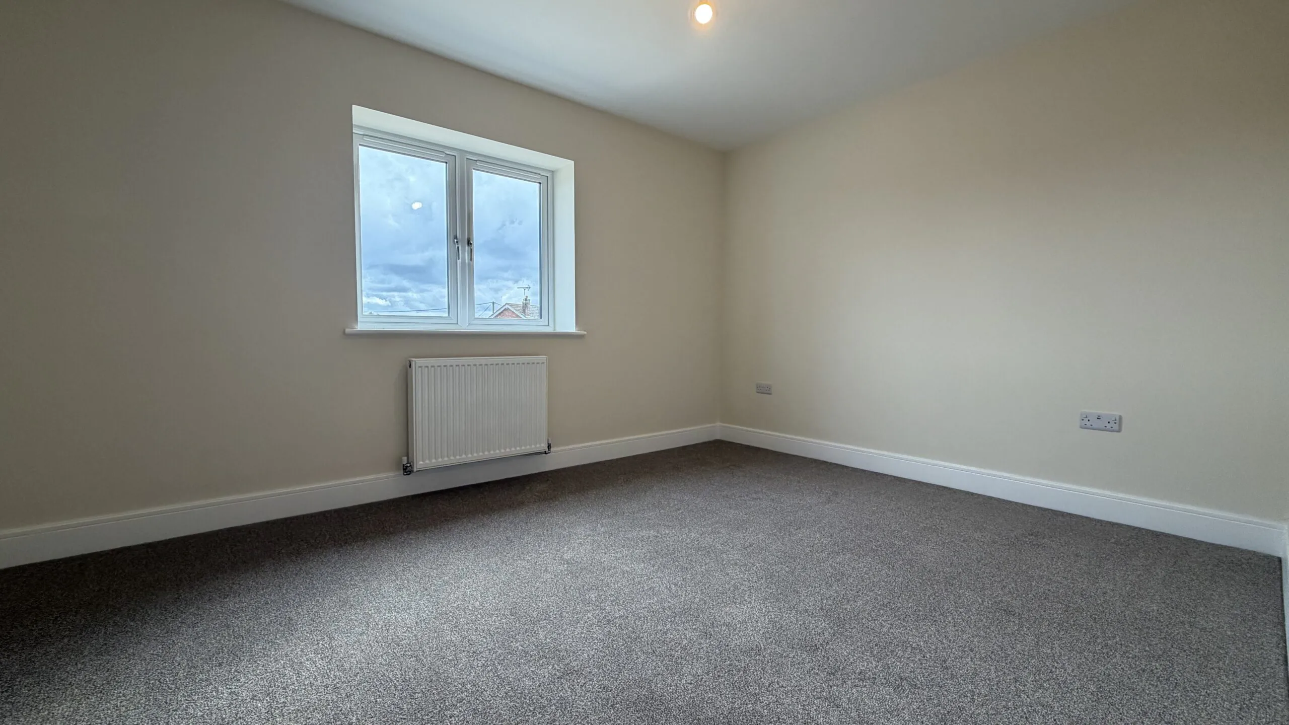 The Caister at Petrella Place – Bedroom 1 with neutral décor, fitted carpet, double window and radiator beneath.