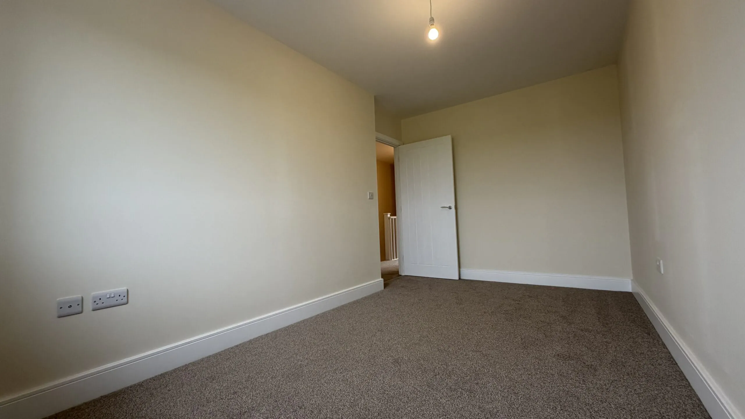 The Caister at Petrella Place – Bedroom 2 alternate view showing neutral décor, fitted carpet, ceiling pendant light and the open door leading to the landing.