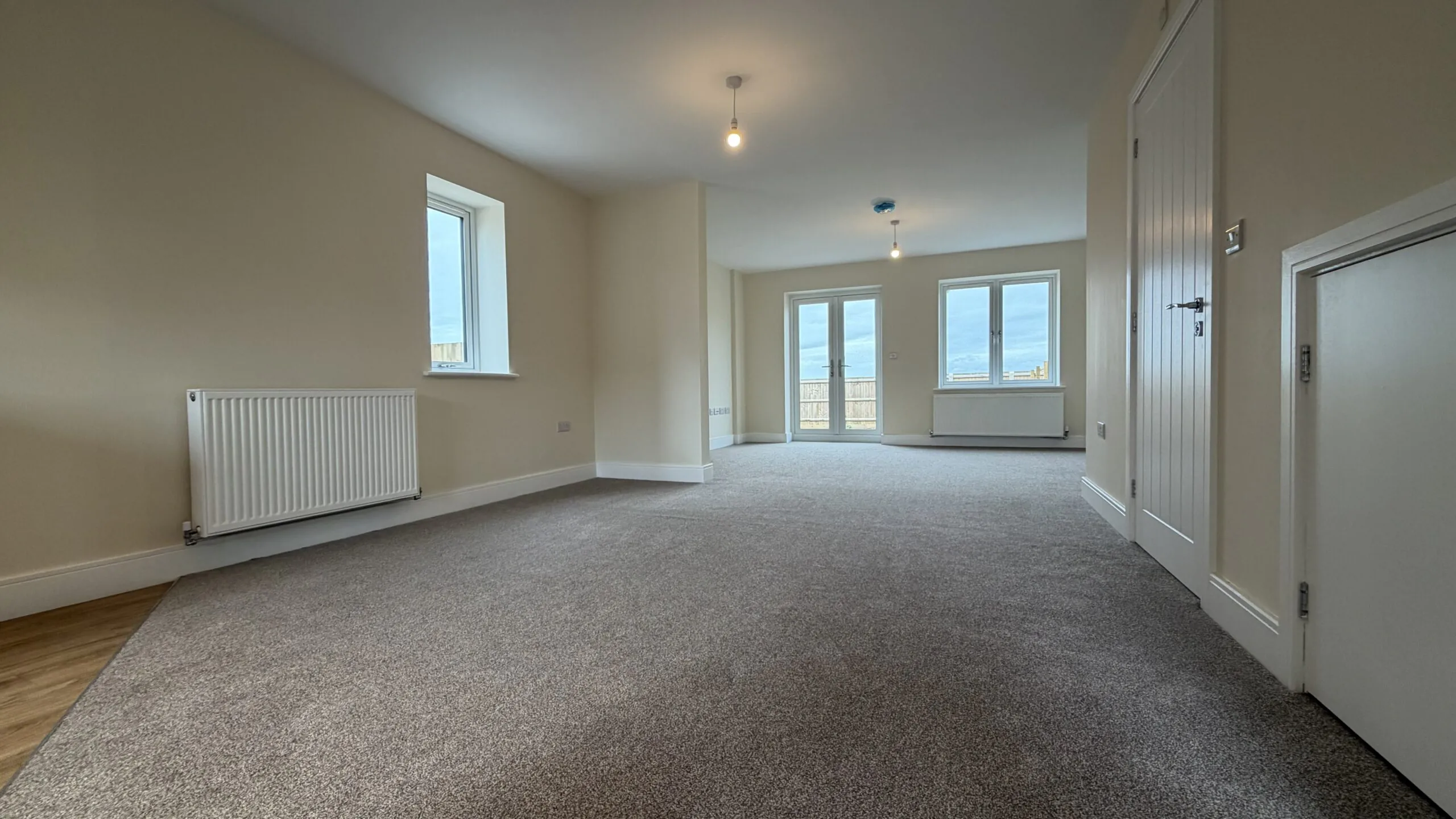 The Caister at Petrella Place – open-plan dining and living room with neutral décor, fitted carpet, side window, and rear French doors with a second rear window bringing in natural light.