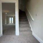 The Caister at Petrella Place – entrance hallway with carpeted stairs, neutral décor and a doorway through to the open-plan living space with French doors beyond.