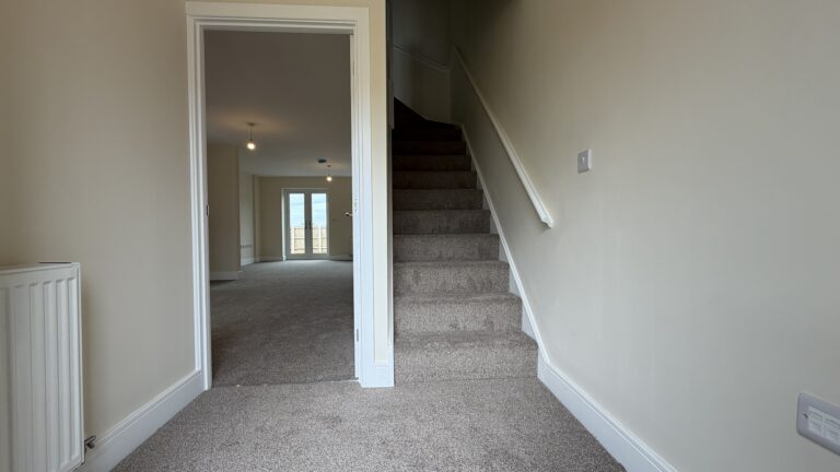 The Caister at Petrella Place – entrance hallway with carpeted stairs, neutral décor and a doorway through to the open-plan living space with French doors beyond.