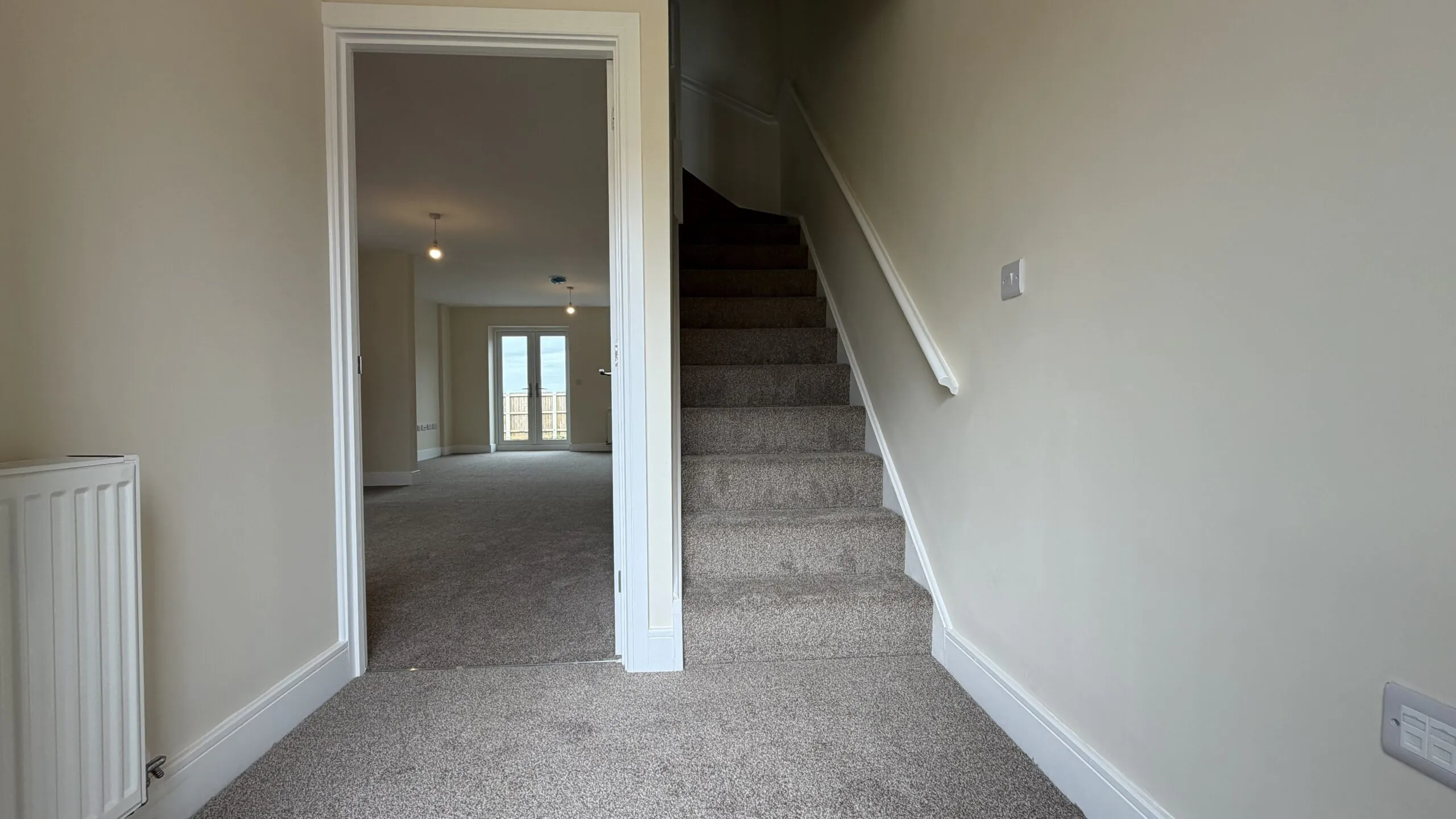 The Caister at Petrella Place – entrance hallway with carpeted stairs, neutral décor and a doorway through to the open-plan living space with French doors beyond.