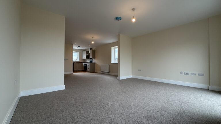 The Caister at Petrella Place – living area looking through to the dining space and kitchen, with neutral décor, fitted carpet, pendant lighting and a side window.