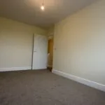 The Caister at Petrella Place – Bedroom 2 alternate view showing carpeted flooring, neutral décor and the doorway out to the landing.