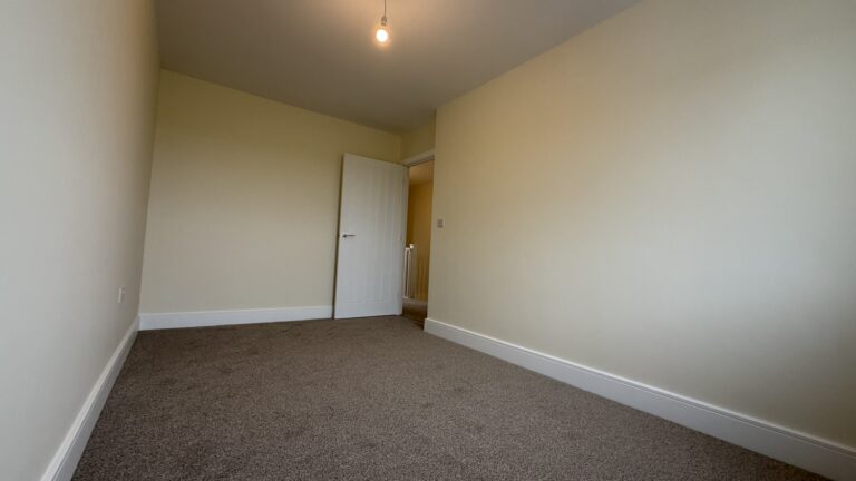 The Caister at Petrella Place – Bedroom 2 alternate view showing carpeted flooring, neutral décor and the doorway out to the landing.