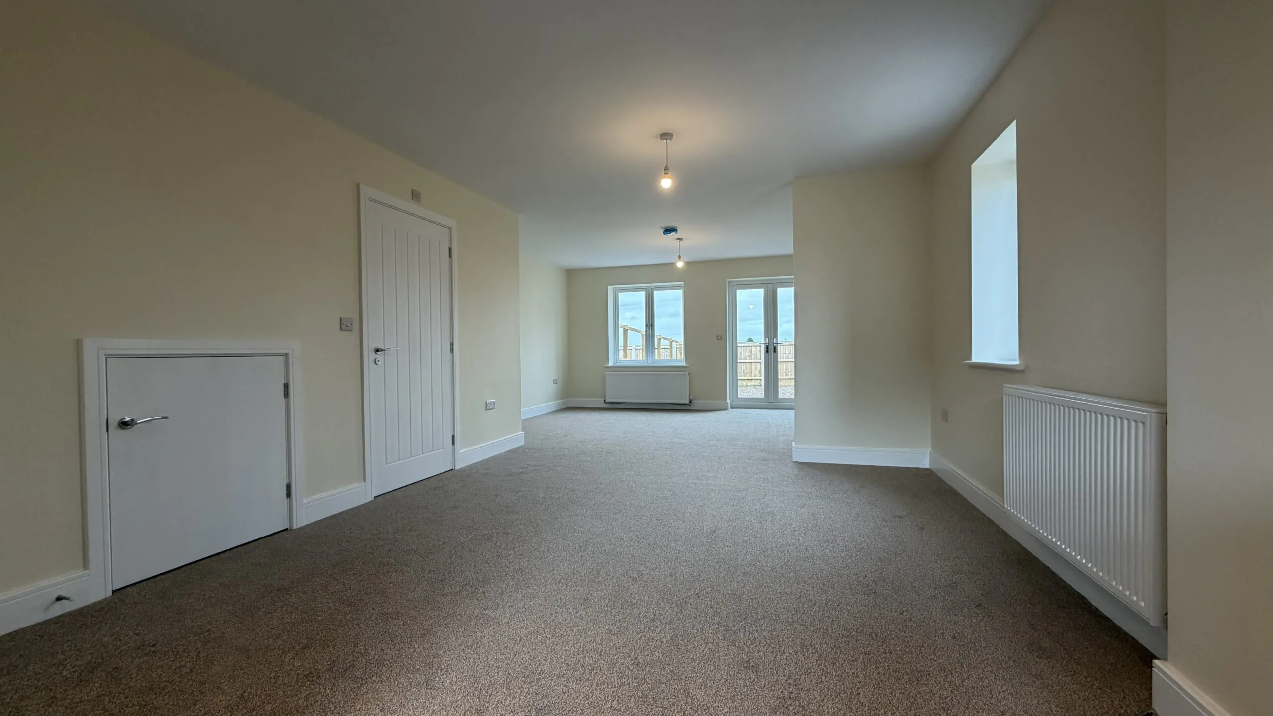 The Caister at Petrella Place – open-plan dining area looking toward the living space with neutral décor, carpeted floor, and window and French doors to the rear garden.