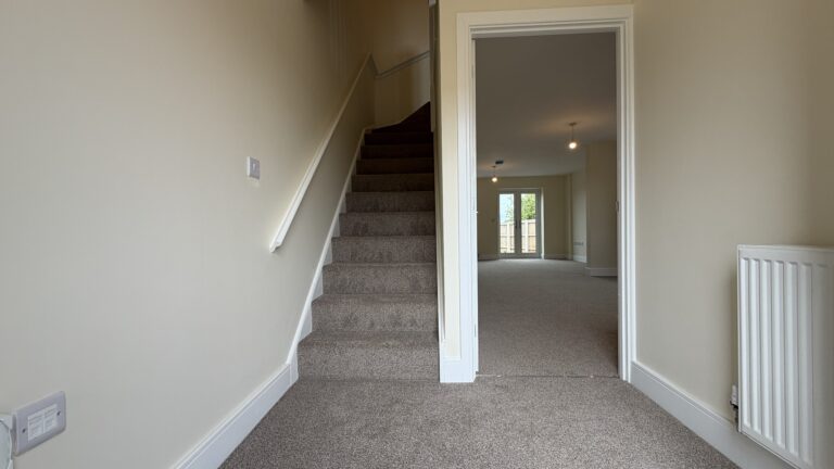 The Caister at Petrella Place – entrance hallway with carpeted stairs, neutral décor and doorway through to the living area with garden doors beyond.