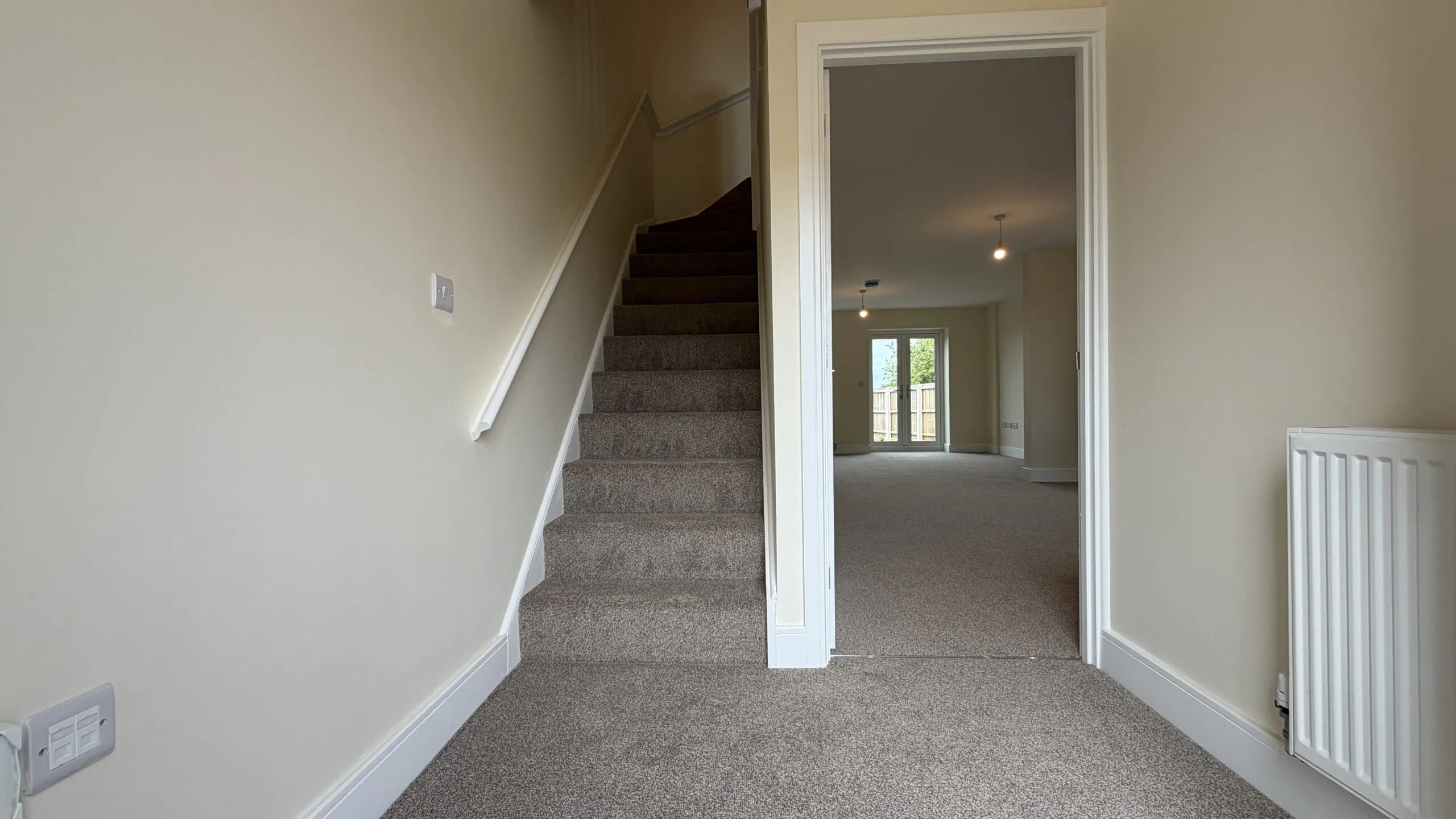 The Caister at Petrella Place – entrance hallway with carpeted stairs, neutral décor and doorway through to the living area with garden doors beyond.