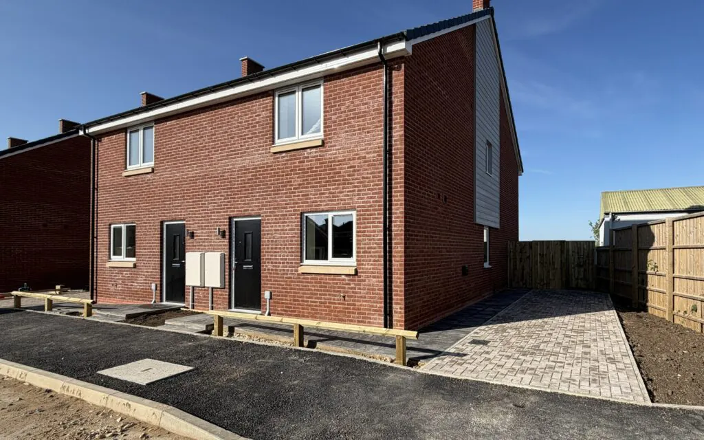 External view of Petrella Place Plots 21 (left) and 22 (right), a pair of new red-brick semi-detached homes with front doors, windows, paved driveway to Plot 22 and soft landscaping areas to be completed.