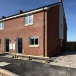 External view of Petrella Place Plots 21 (left) and 22 (right), a pair of new red-brick semi-detached homes with front doors, windows, paved driveway to Plot 22 and soft landscaping areas to be completed.
