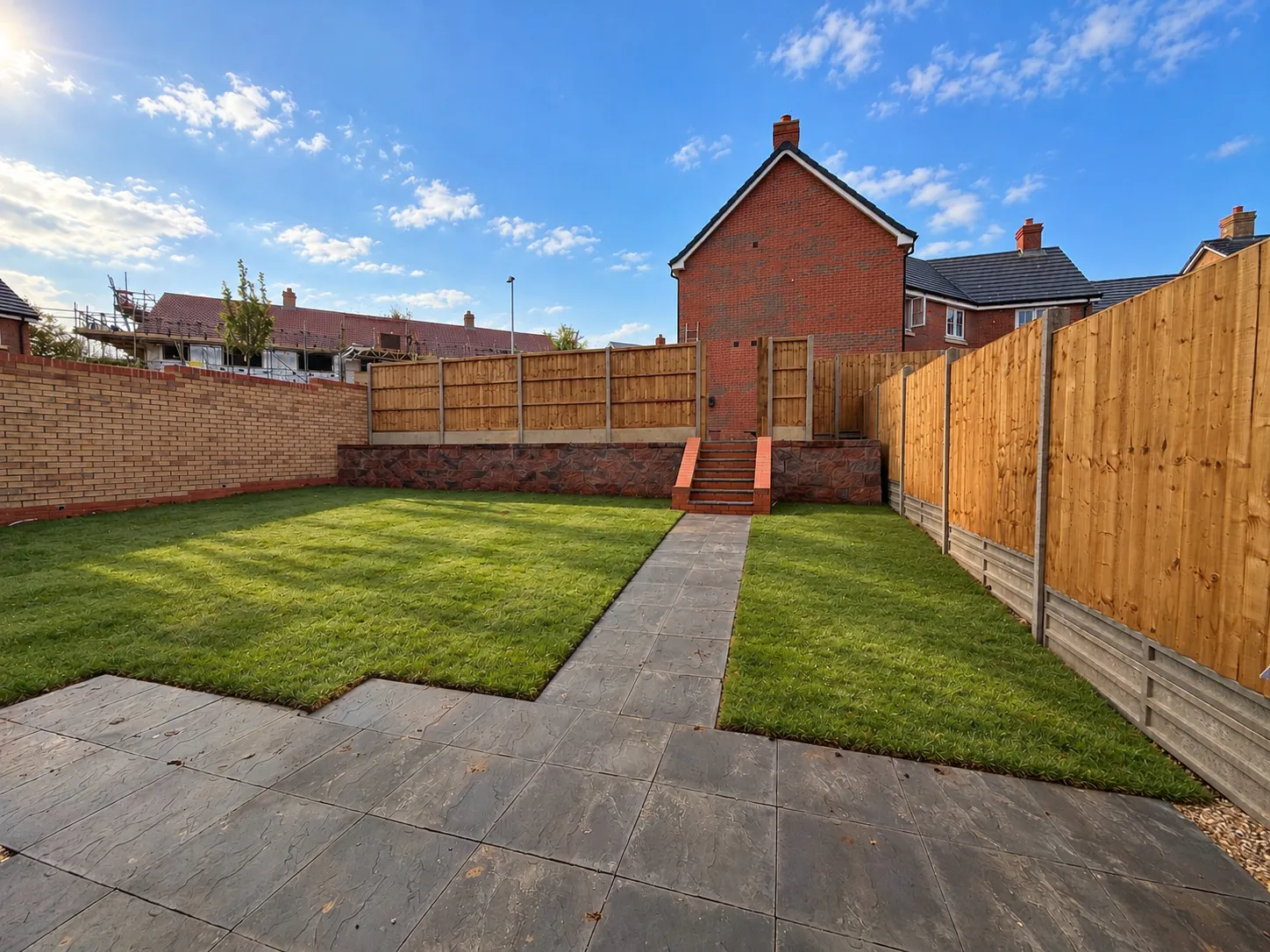 Enclosed rear garden at 34 Warwick Drive featuring a paved patio, lawned garden, secure timber fencing and raised rear section with steps providing additional outdoor space.