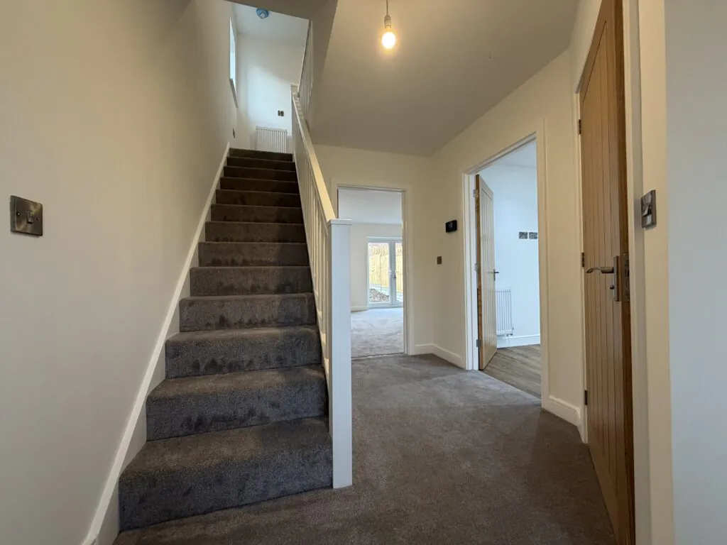 34 Warwick Drive, Washingborough LN4 1UW 4 Entrance hallway at 34 Warwick Drive featuring a carpeted staircase, useful under-stairs storage, access to the kitchen and cloakroom, and views through to the living room and rear garden.