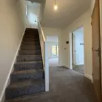 Entrance hallway at 34 Warwick Drive featuring a carpeted staircase, useful under-stairs storage, access to the kitchen and cloakroom, and views through to the living room and rear garden.