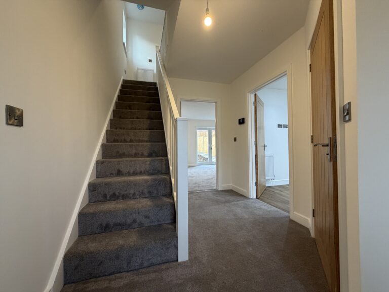 Entrance hallway at 34 Warwick Drive featuring a carpeted staircase, useful under-stairs storage, access to the kitchen and cloakroom, and views through to the living room and rear garden.