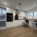 Contemporary kitchen at 34 Warwick Drive showcasing integrated AEG appliances including a fridge freezer, dishwasher and washing machine, alongside modern white cabinetry and wood-effect worktops.