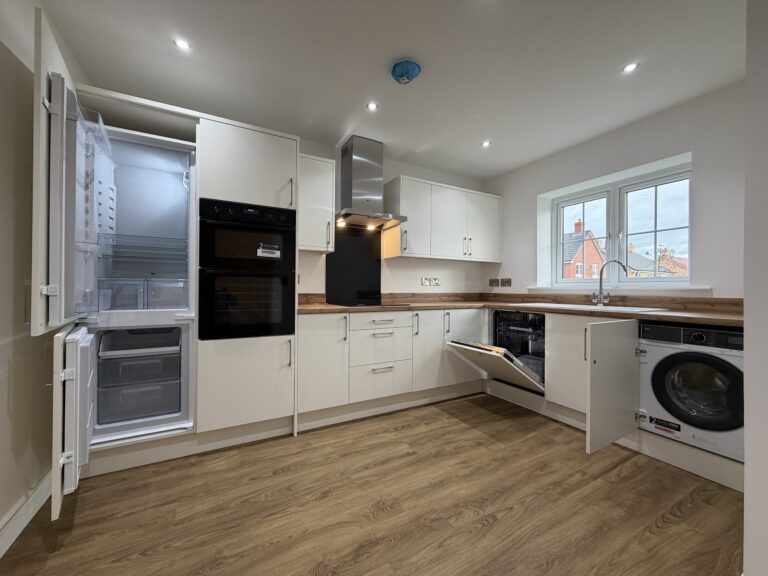 Contemporary kitchen at 34 Warwick Drive showcasing integrated AEG appliances including a fridge freezer, dishwasher and washing machine, alongside modern white cabinetry and wood-effect worktops.