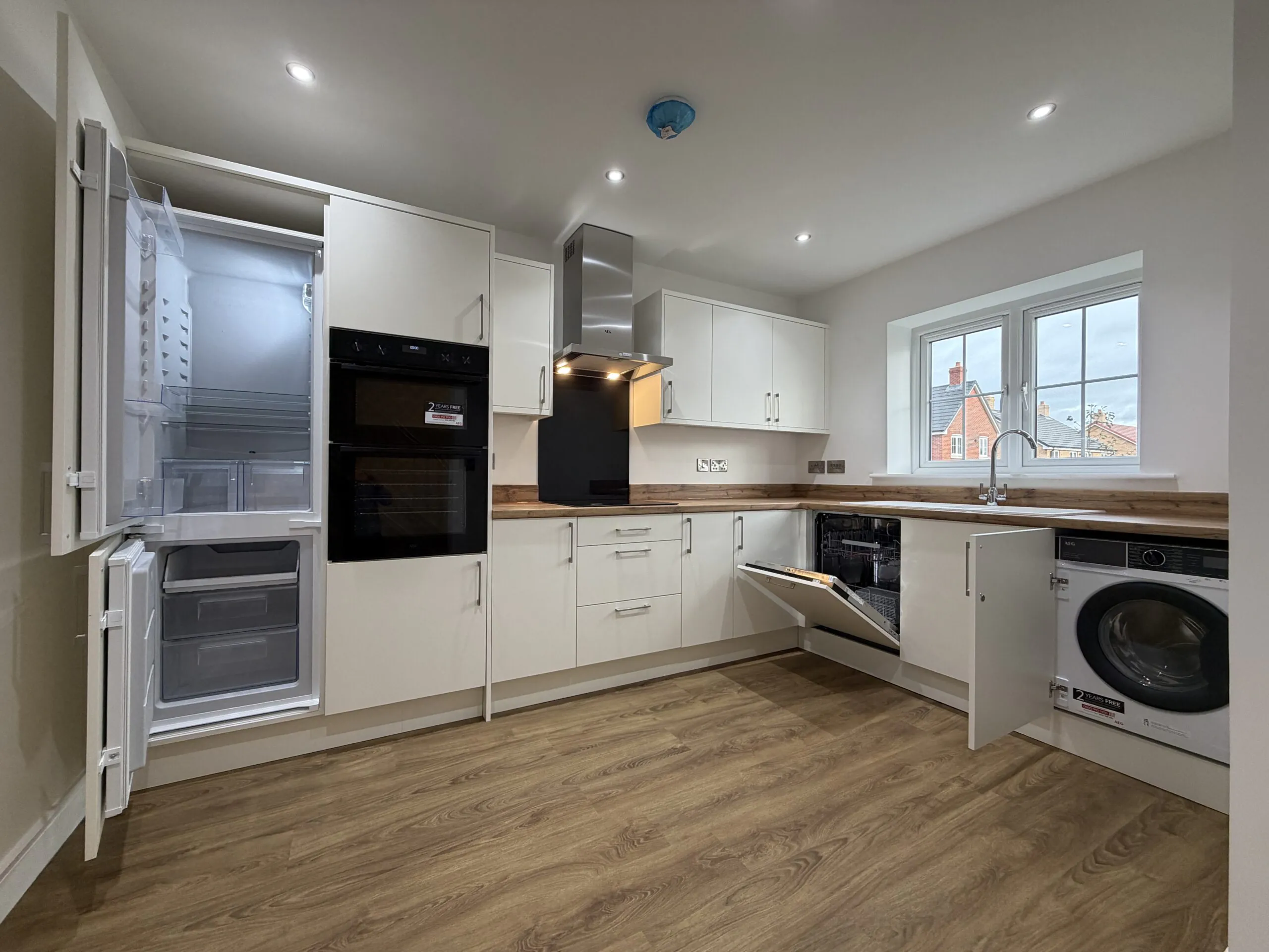 Contemporary kitchen at 34 Warwick Drive showcasing integrated AEG appliances including a fridge freezer, dishwasher and washing machine, alongside modern white cabinetry and wood-effect worktops.