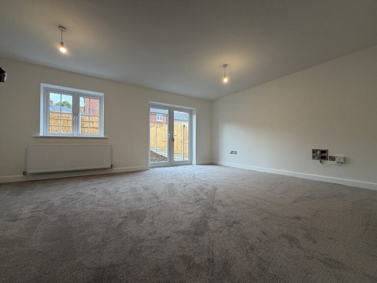 Spacious living room at 34 Warwick Drive featuring soft carpeting, generous floor space, a rear-facing window and French doors opening onto the enclosed garden.
