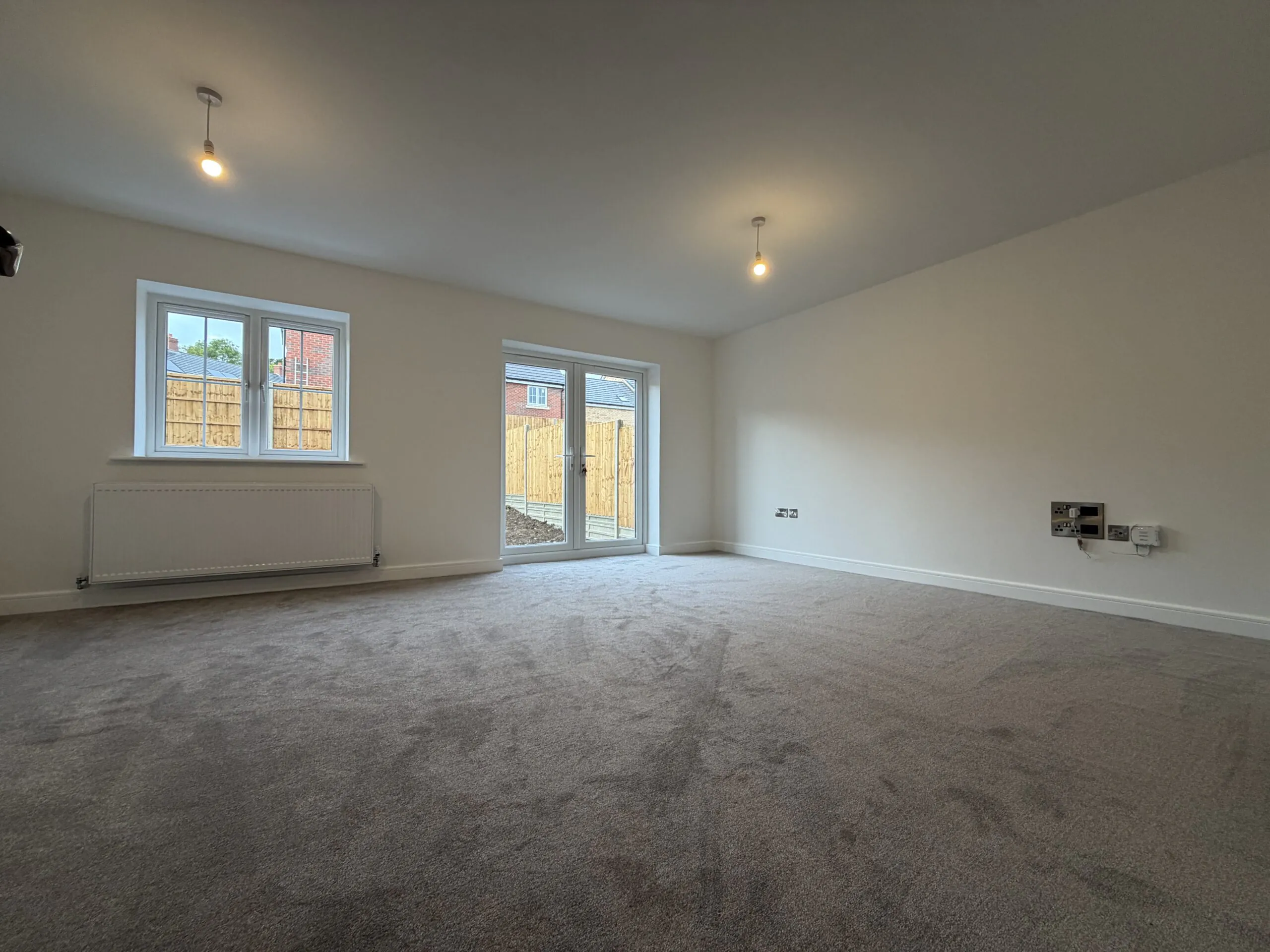 Spacious living room at 34 Warwick Drive featuring soft carpeting, generous floor space, a rear-facing window and French doors opening onto the enclosed garden.