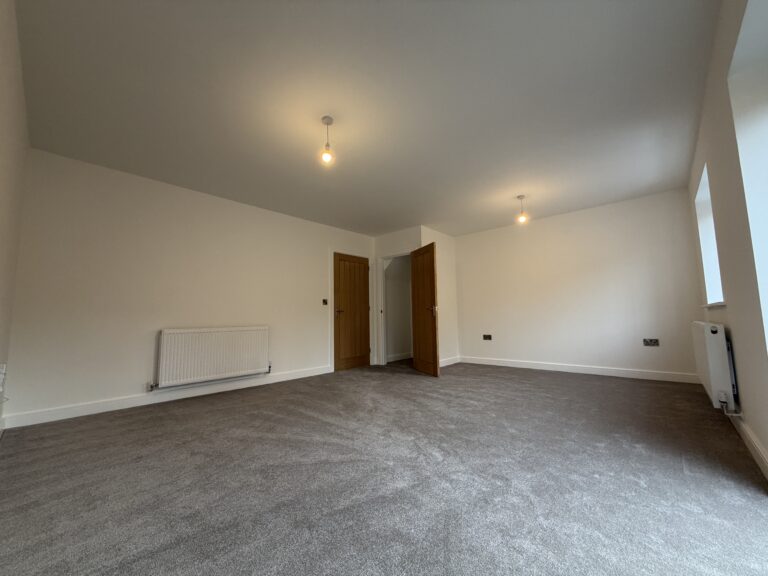 Spacious living room at 34 Warwick Drive featuring soft grey carpeting, a bright dual-aspect layout and ample space for both lounge and dining furniture.