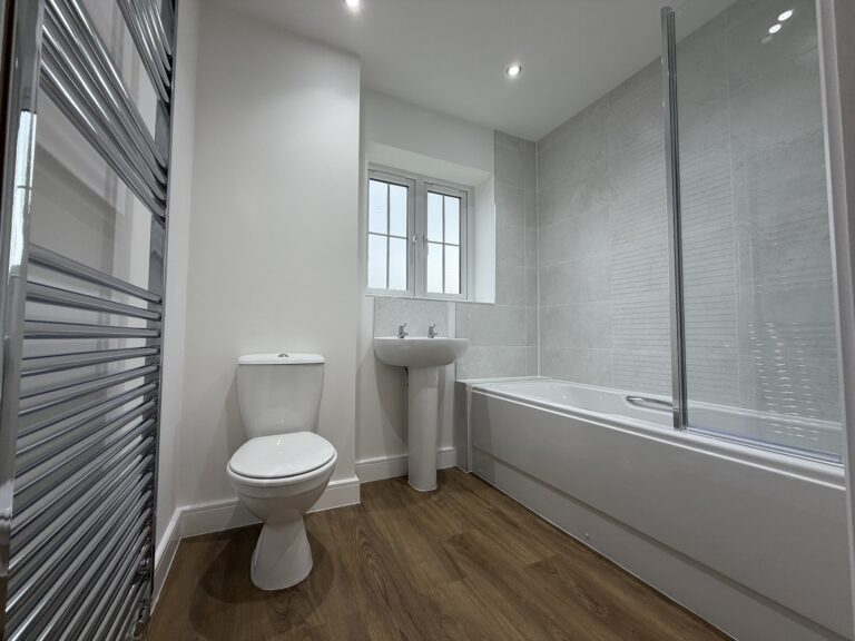Family bathroom at 34 Warwick Drive featuring a contemporary white suite, bath with shower and glazed screen, pedestal wash basin, WC and chrome heated towel rail.