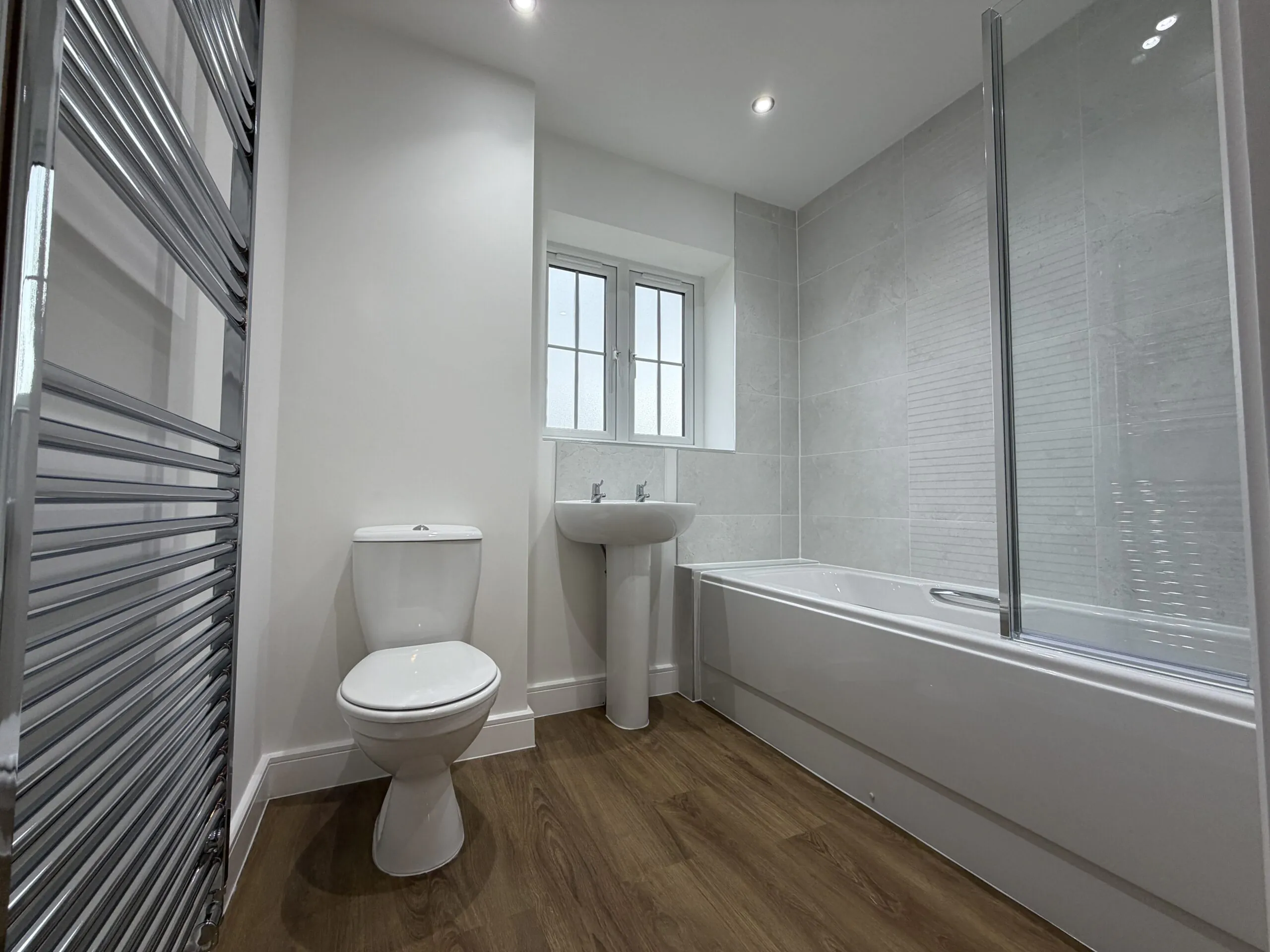 Family bathroom at 34 Warwick Drive featuring a contemporary white suite, bath with shower and glazed screen, pedestal wash basin, WC and chrome heated towel rail.