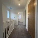 First-floor landing at 34 Warwick Drive featuring a carpeted floor, staircase with white balustrade, built-in storage cupboard and access to all three bedrooms and the family bathroom.