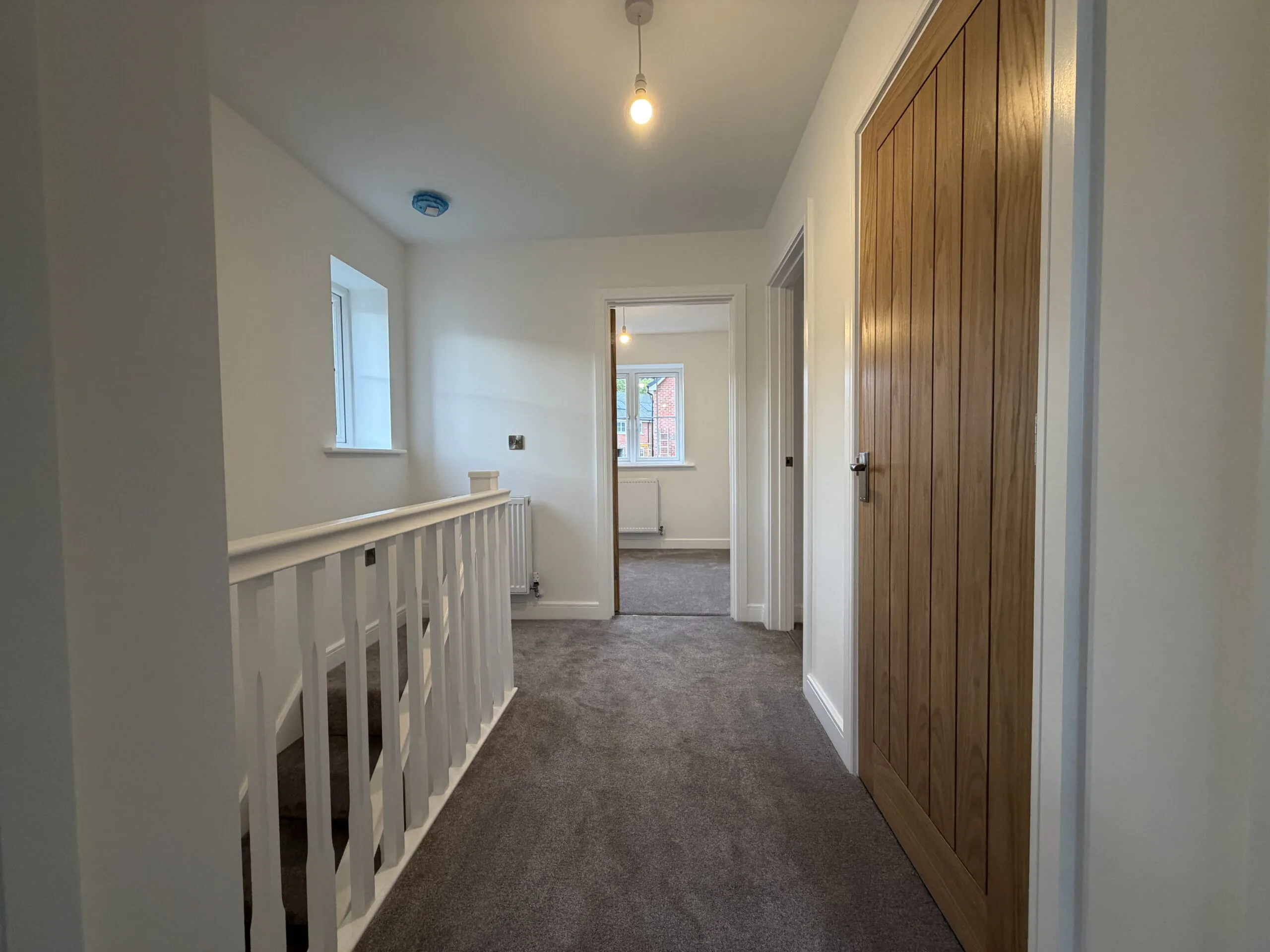 First-floor landing at 34 Warwick Drive featuring a carpeted floor, staircase with white balustrade, built-in storage cupboard and access to all three bedrooms and the family bathroom.