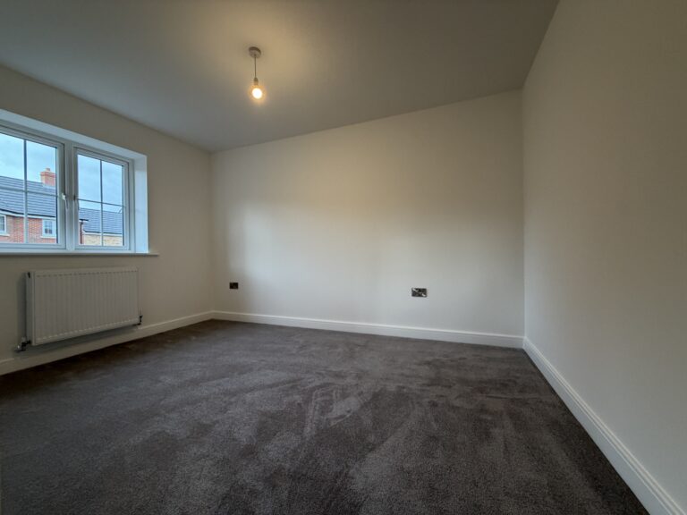 Bedroom Two at 34 Warwick Drive featuring soft grey carpeting, a rear-facing window providing natural light and a spacious layout suitable for a double bed and additional furniture.